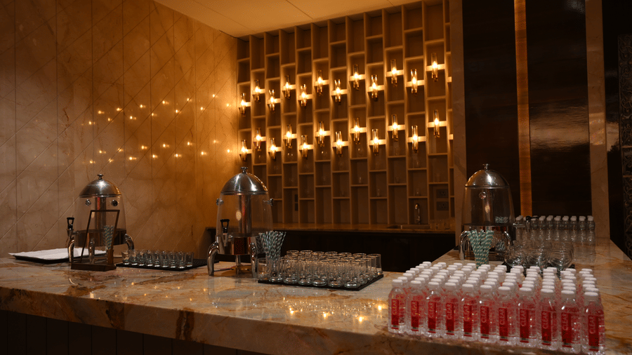 A long refreshment counter features glass beverage dispensers and stacks of cups in the Lambic banquet hall at Praveg's Grand Eulogia, Ahmedabad.