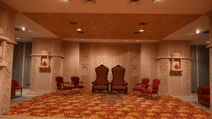 2 large decorative chairs sit on a raised stage with a patterned carpet inside the Lambic banquet hall at Praveg's Grand Eulogia, Ahmedabad.