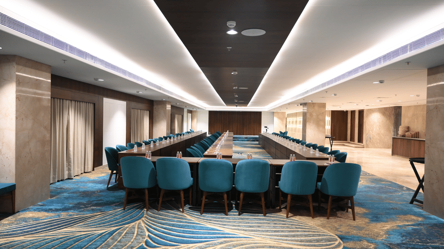 A hollow square meeting layout with multiple chairs faces the front of a modern corporate room in the Sky Lounge at Praveg's Grand Eulogia, Ahmedabad.