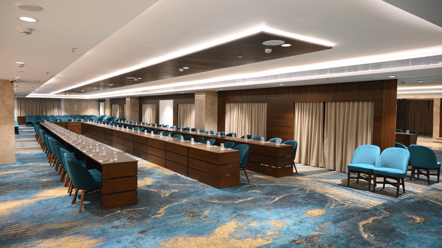 A long, narrow wooden conference desk stretches across the large event room with wavy carpet patterns in the Sky Lounge at Praveg's Grand Eulogia, Ahmedabad.