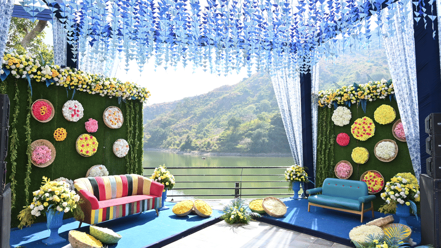 Blue floral mandap with colourful sofa seating and green hills as a backdrop at Via Lakhela Resort & Spa, a wedding resort in Kumbhalgarh.