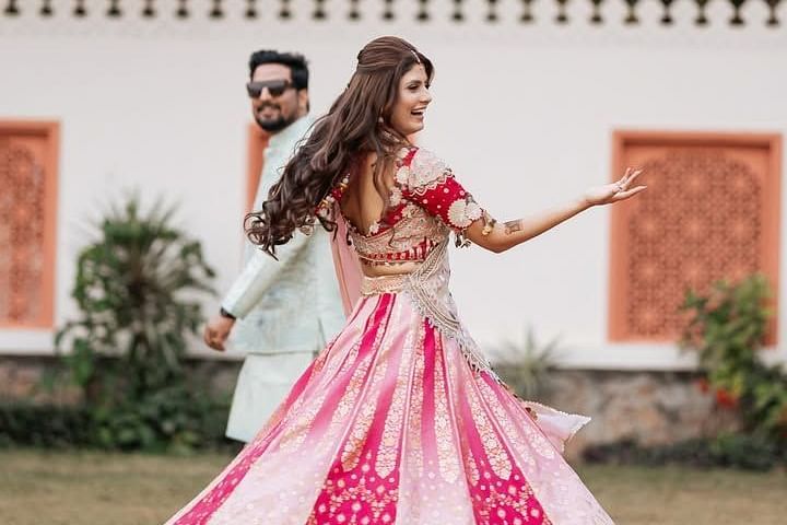 The bride twirls joyfully in a lehenga while the groom follows, smiling, in a picturesque outdoor setting. - Umaid Palace - A Lakeside Heritage Palace Resort