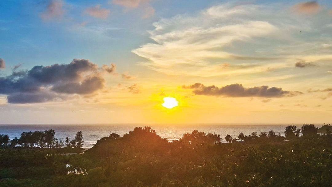 The sunrise view over the trees and beach, set against a slightly cloudy sky, offers a serene scene at Cloud9 Sarovar Premiere, Palolem Goa