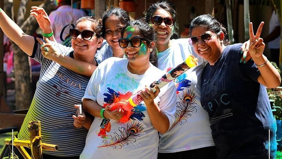 A group of people with vibrant colors on their faces, celebrating Holi at Themis Mudhouse, radiating joy and festivity.