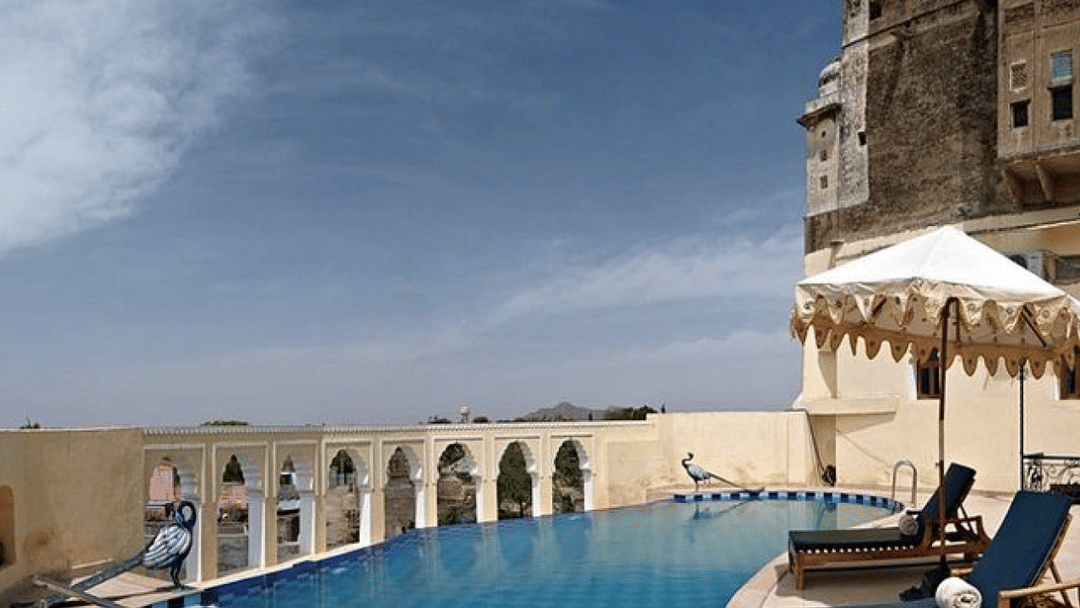 A luxurious pool with patterned tiles stretches alongside a historic fort building at Fort Barli, offering a blend of relaxation and heritage.