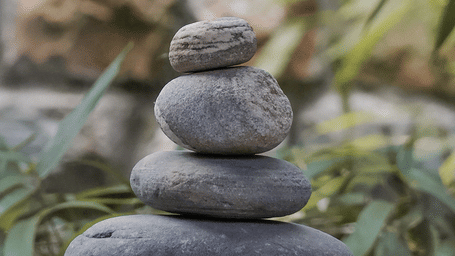 A neat vertical stack of four smooth river stones balanced outdoors in a serene natural setting at Kavya Himalayas.