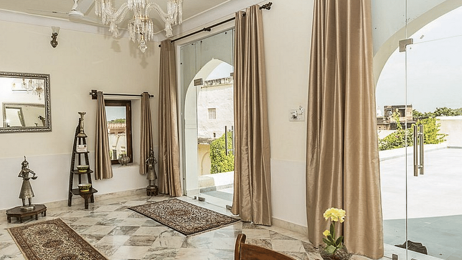 A bright, airy room at Fort Barli, with a chandelier, marble floors, and draped doorways leading to an outdoor space, blends elegance with open design.