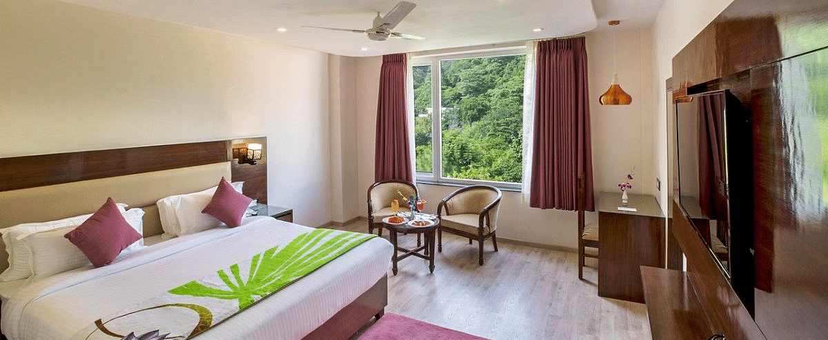 Full view shot of the Premium Room at Regenta Inn DLS featuring a double bed overlooking the lush green views from the window.