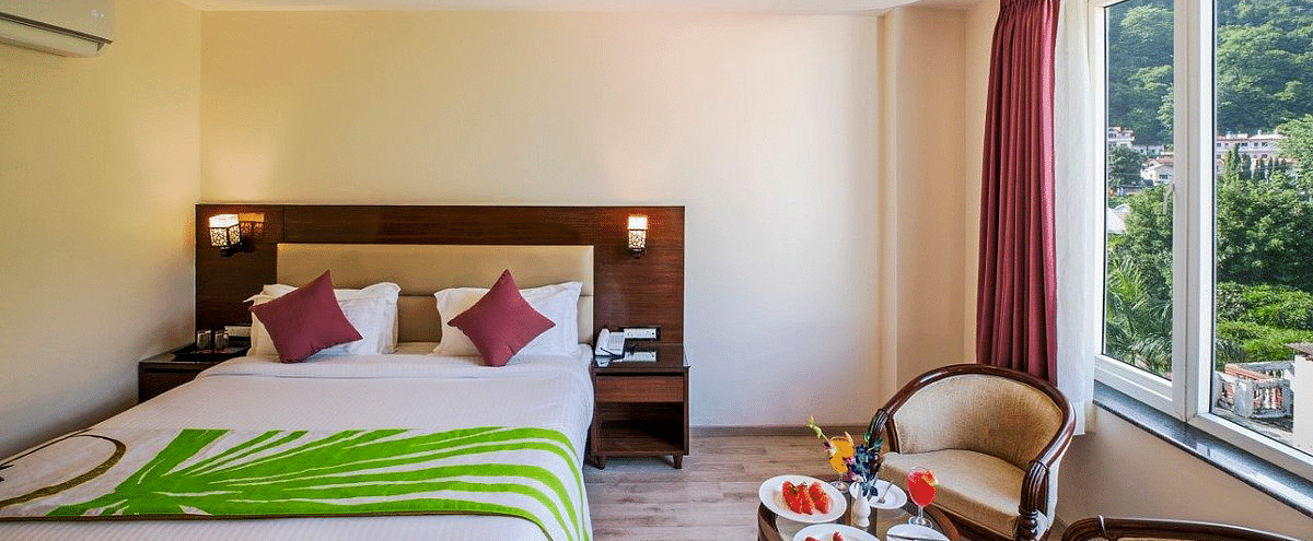 A double bed kept in the Premium Room with a common seating area in front of the window at Regenta Inn DLS.