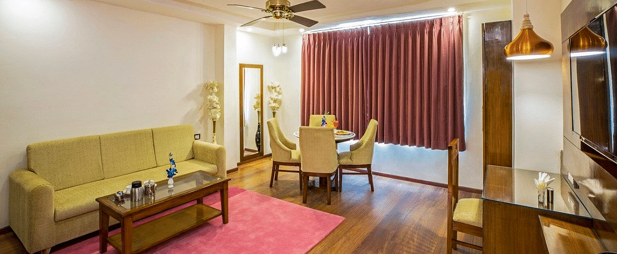 The living area of the Suite with the window covered with maroon curtains at Regenta Inn DLS.