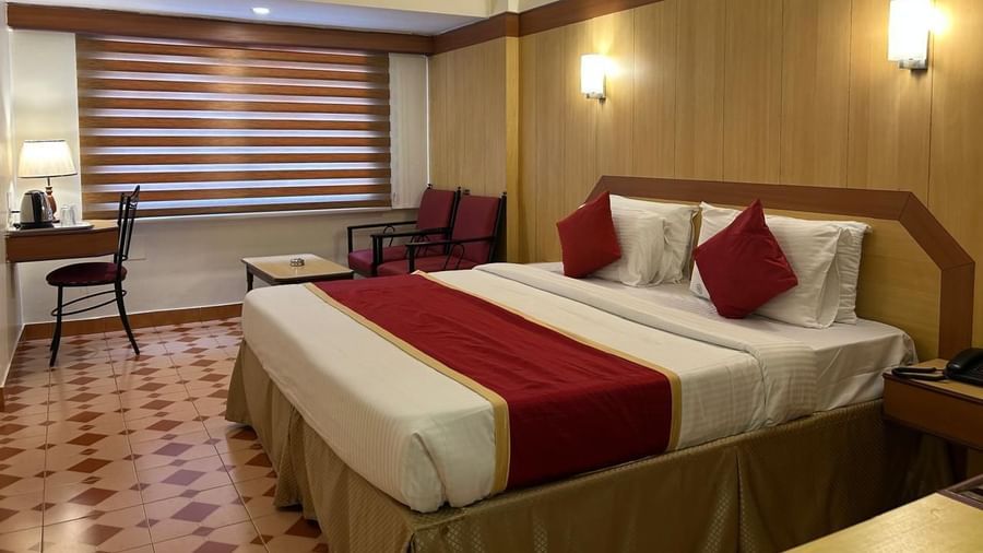 Spacious guest room at Hotel Swagath, Bangalore with two twin beds, cushioned headboards, and warm lighting.