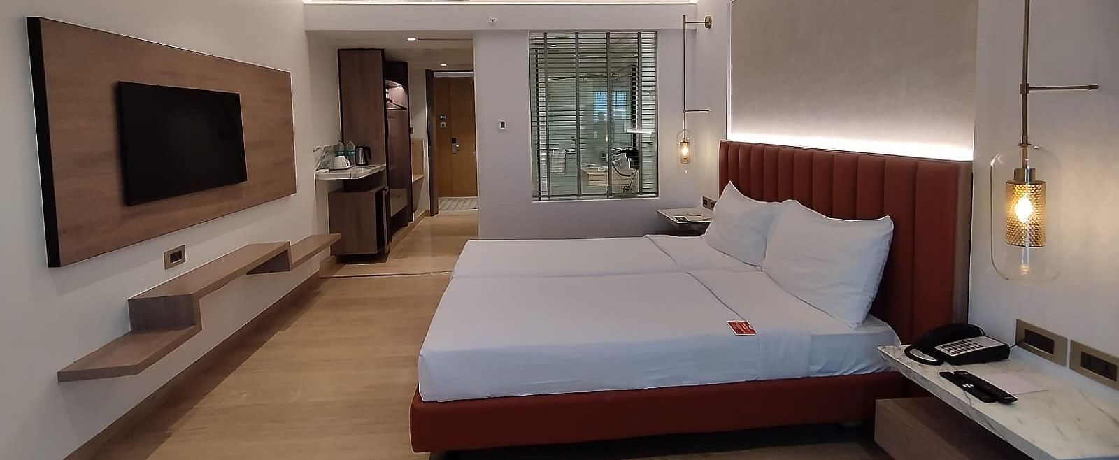 A well-lit, wooden floored, executive room in Mirage Hotel, featuring twin beds with decorative head-rest and a wooden panelled entertainment unit.