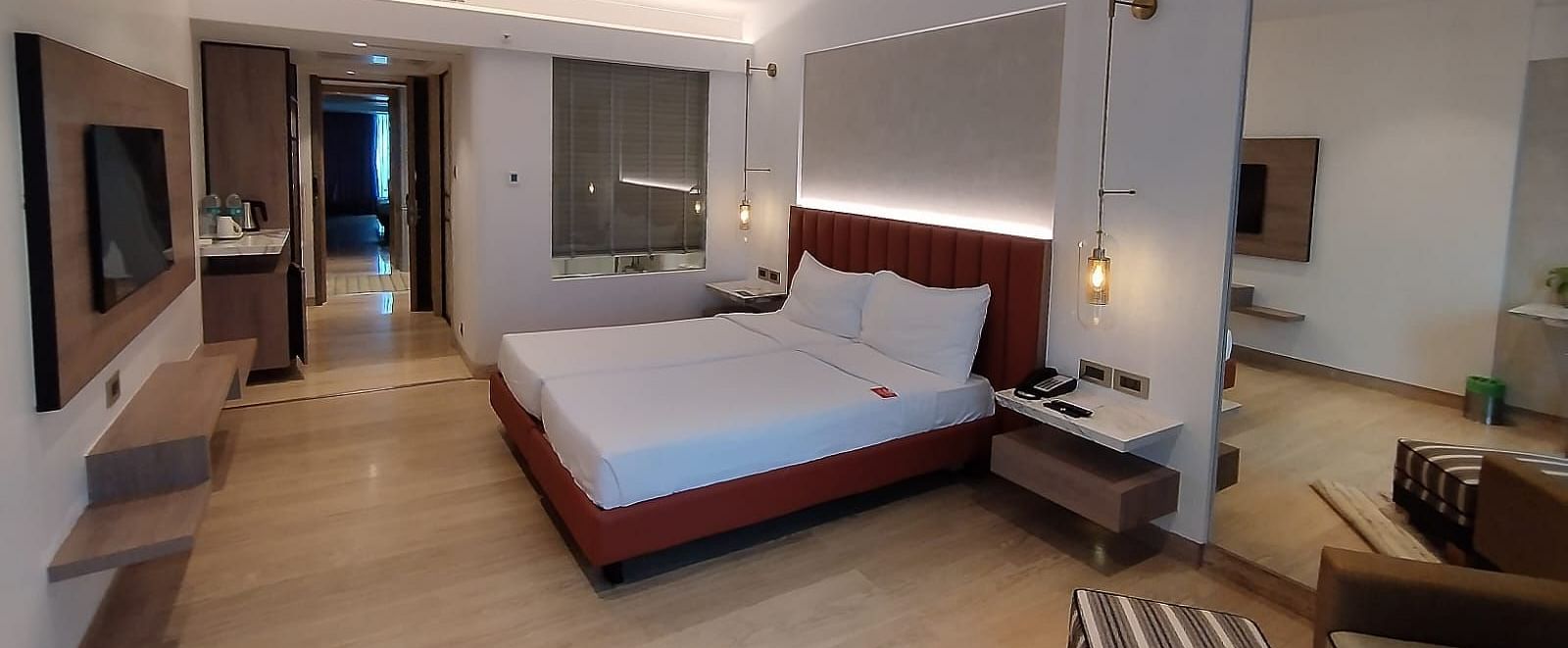 A warmly lit executive bedroom in Mirage Hotel, featuring twin beds, a large mirror, lounge chairs, and an entertainment unit.