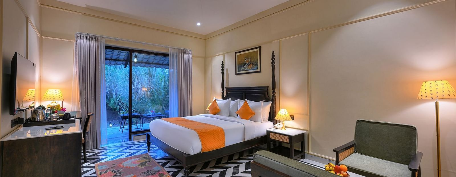 A well-lit Superior Cottage at Singhvilas with a four-poster bed, a black and white geometric floor, a work desk with amenities, and a balcony offering a view of the outdoors.
