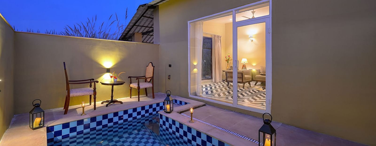 A serene outdoor space of Premium Suite Cottage featuring a tiled plunge pool, cosy seating, and warm lanterns, illuminated by a twilight sky - Singhvilas, Ranthambore