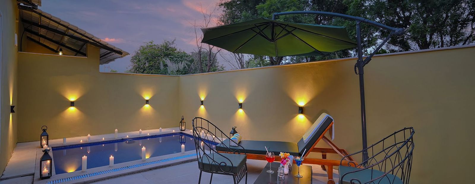 A secluded patio in Luxury Suite Cottage with a small, illuminated pool, lounge chairs, an umbrella, and outdoor lighting at dusk - Singhvilas, Ranthambore