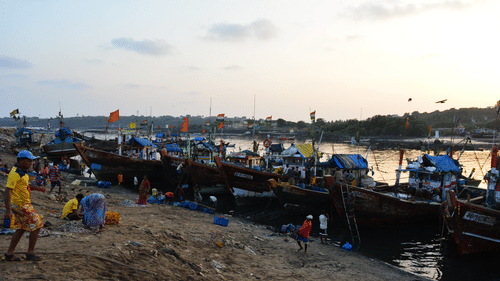 A row of boat, anchored at a bank with people walking about and the sea and sky in the background.