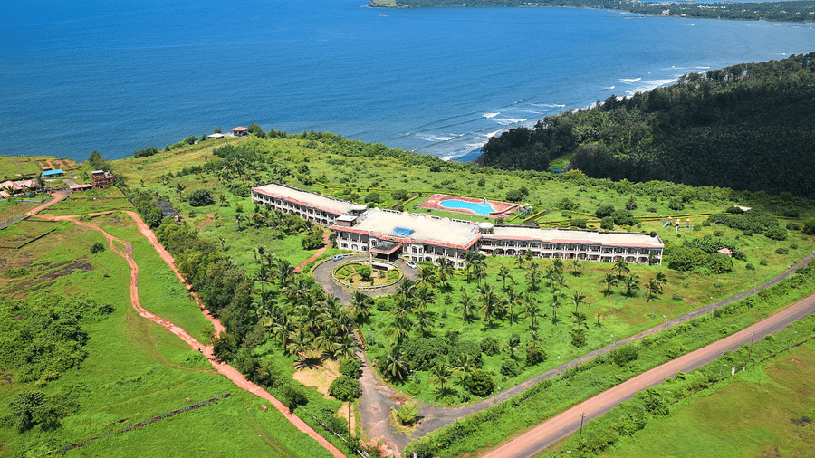 Aerial view of Kohinoor Samudra Beach Resort, Ratnagiri, overlooking the Arabian Sea, with lush green landscapes, landscaped gardens, and an outdoor swimming pool.