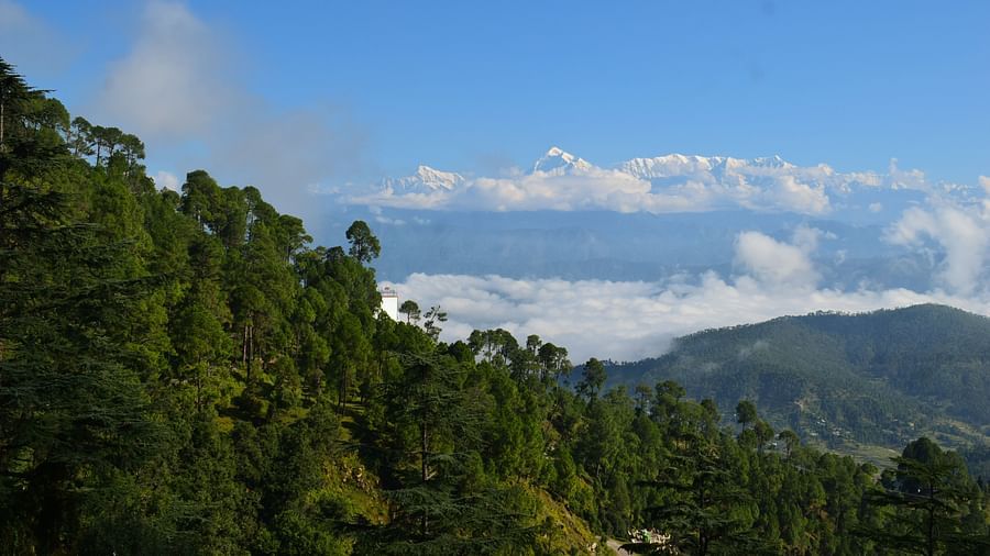 Panoramic view of lush green mountains with a winding road leading to a distant village.