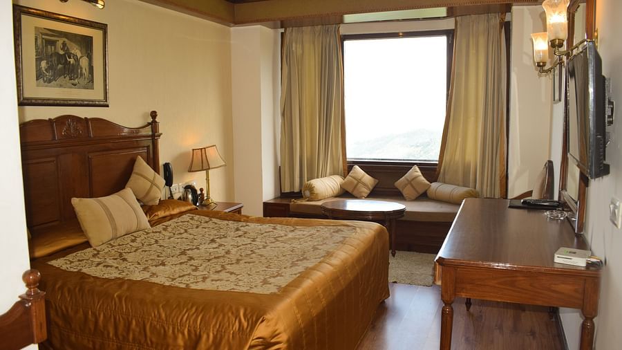 Himalayan View Room in Kausani with a large bed opposite a desk and a sofa placed in front of a window - Sun N Snow Inn, Kausani