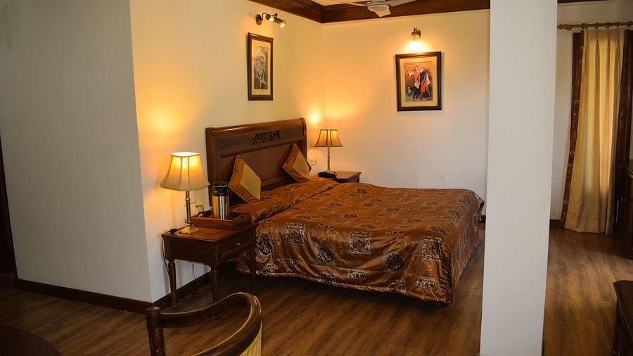 A wide view of a bedroom with a double bed with side lamps on both sides of the bed and a work desk and chair on the other side of the room - Sun N Snow Inn, Kausani
