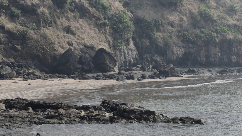 An overview of Alibaug beach for the perfect Long Weekend Vacation near Mumbai, featuring rocks and mountains.