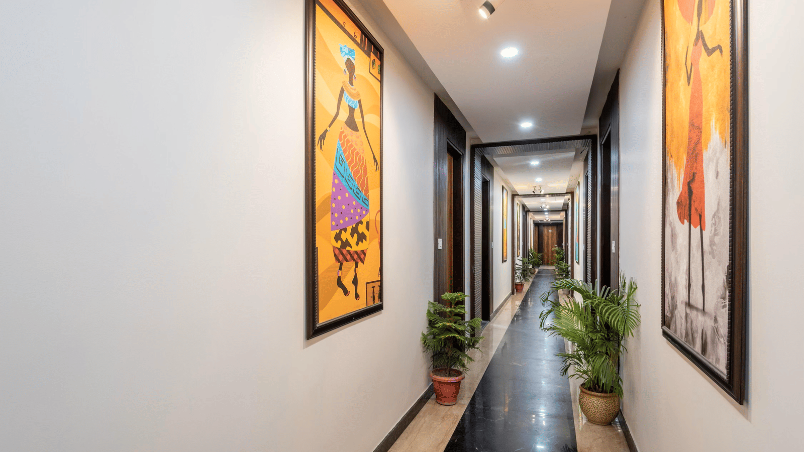 A long hotel hallway with wall artworks, potted plants, and overhead lighting at Perfectstayz Premium Shanti Heritage, Haridwar