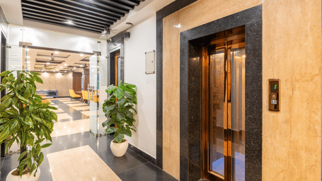 A hotel lobby hallway featuring a glass elevator and potted plants at Perfectstayz Premium Shanti Heritage, Haridwar