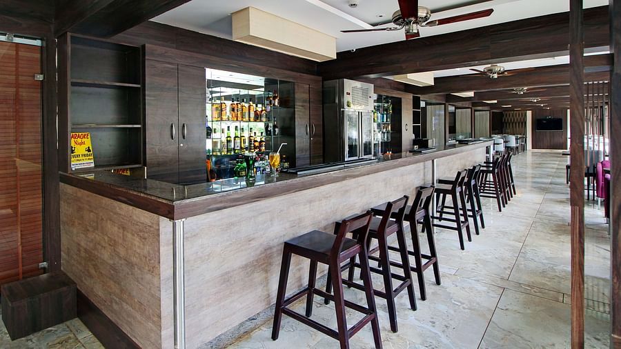An elegant hotel bar with a dark wood counter and matching stools, shelves of various beverages, and a karaoke night promotion sign