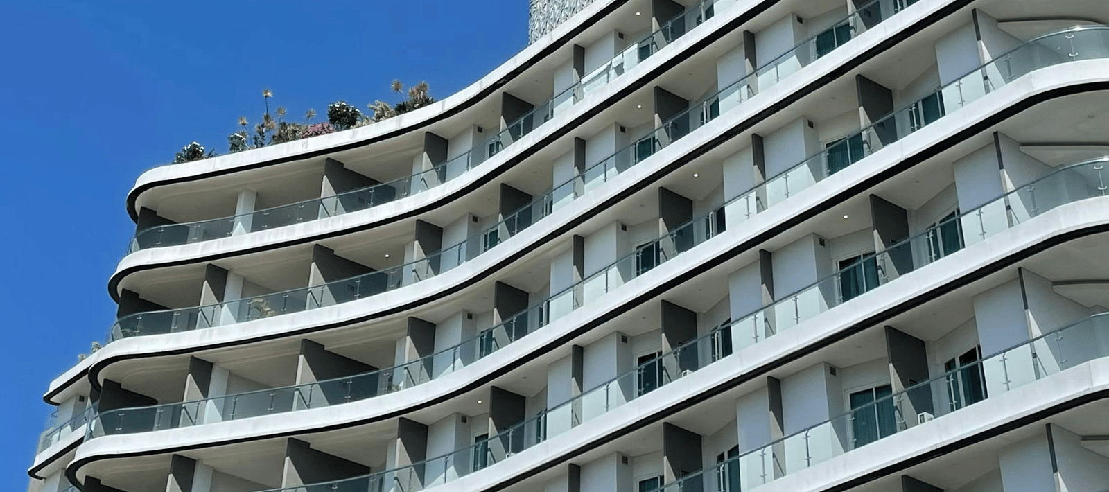 A tall, modern hotel building with curved white balconies against a clear blue sky.