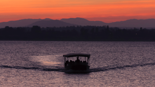 A boat cruising through a river during sunset with the hills visible in the background.