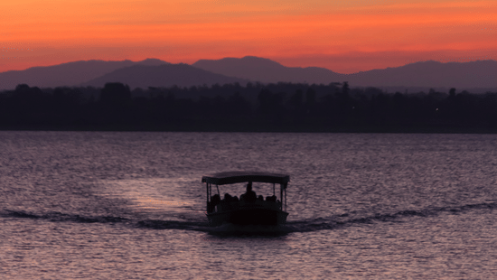 A boat cruising through a river during sunset with the hills visible in the background.
