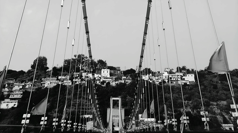A black and white vertical perspective looking down the length of a long suspension bridge.