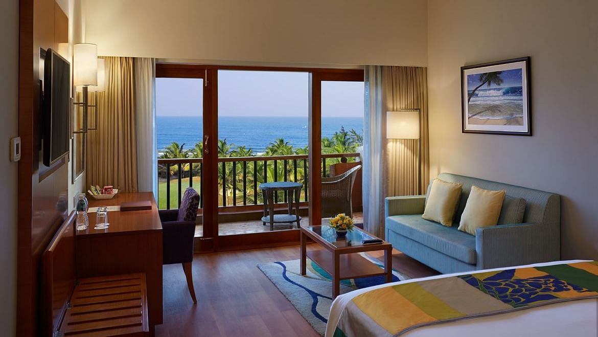 a double bed with a sofa, table, lamps and tv in view inside Ocean front view - Caravela Beach Resort Goa