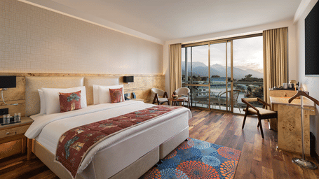 iew of a room at Infinitea Centric Dharamshala by Zenq with a king bed, wooden flooring, colourful rug, and a sweeping mountain view beyond.