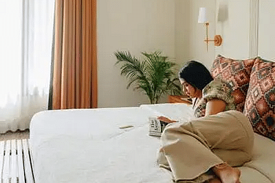 A woman lying on a bed with white linen, potted plant and a huge windows with curtains at Karma Chalets.