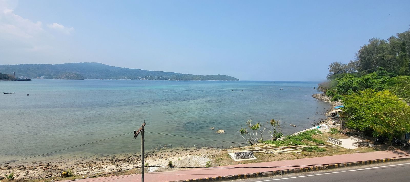 View of the ocean and the road outside 6ix Seashore Hotel, Port Blair along with trees on the shore