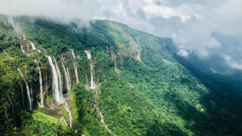 Aerial view of the Seven Sisters Waterfalls cascading down a green cliff face shrouded in mist near Cherrapunji in Meghalaya.