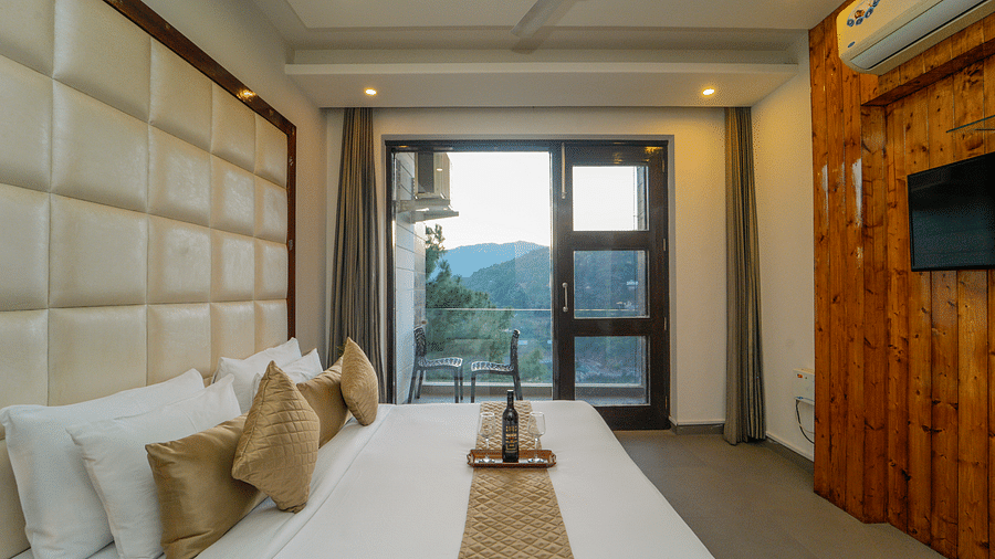The premium room at DLS Whispering Winds featuring a bed with plush bedding and the glass door leading to the balcony with the mountain view