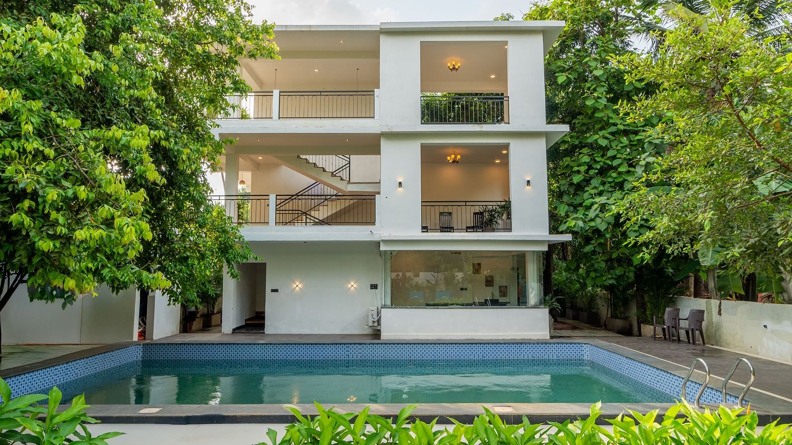 Modern white building with a swimming pool surrounded by greenery at De Soul Santé Hotels & Resorts.