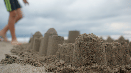 A sand castle at the beach, with a person walking in the background.