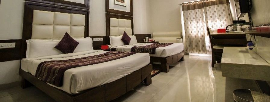 Elegant room with two large beds, table, chair and TV unit at Hotel Emerald, Chandigarh