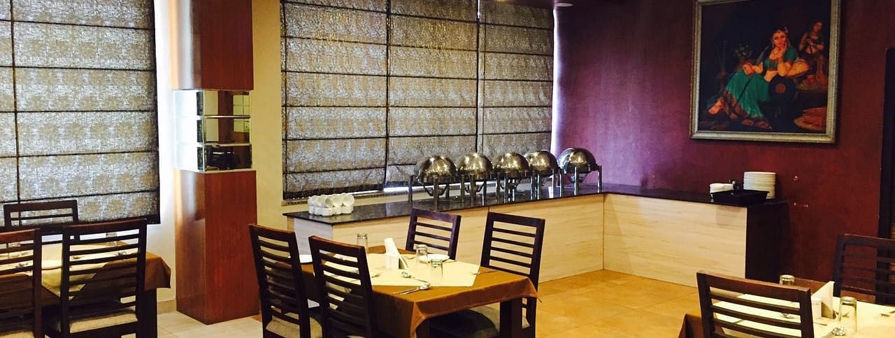 A dining room with a serene ambience, featuring a mix of wooden chairs and tables and a decorative screen - TGI Apple Inn, Jaipur 