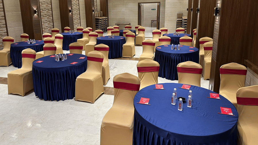 Multiple decorated seating arrangement in a spacious hall featuring round tables and chairs around it at Shyanu Lords Eco Inn Airoli.