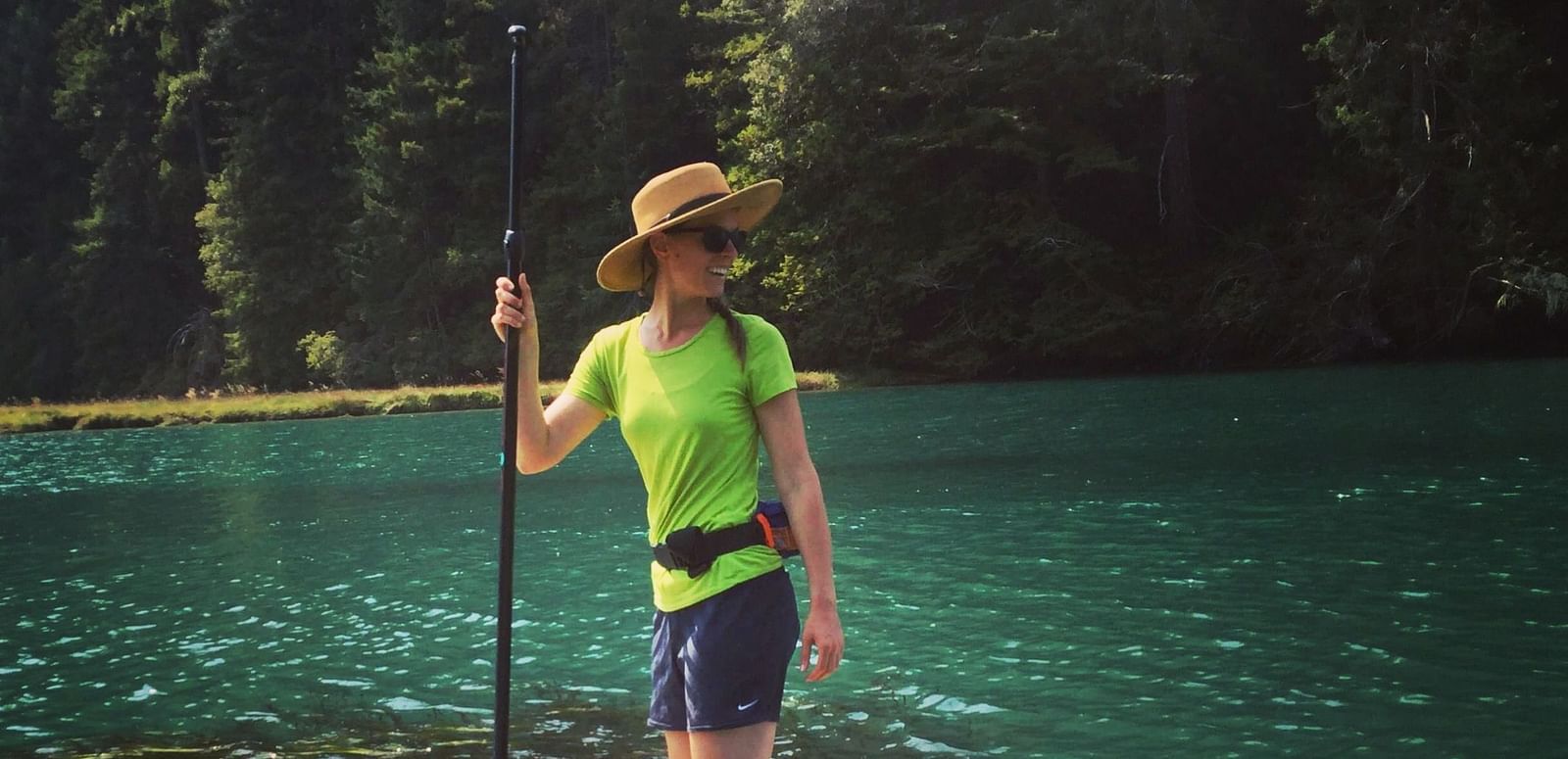 A person standing on a paddleboard in a calm body of water, holding a paddle.