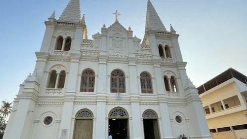 A grand cathedral with twin towers and arched entrances, set against a clear sky and open courtyard.