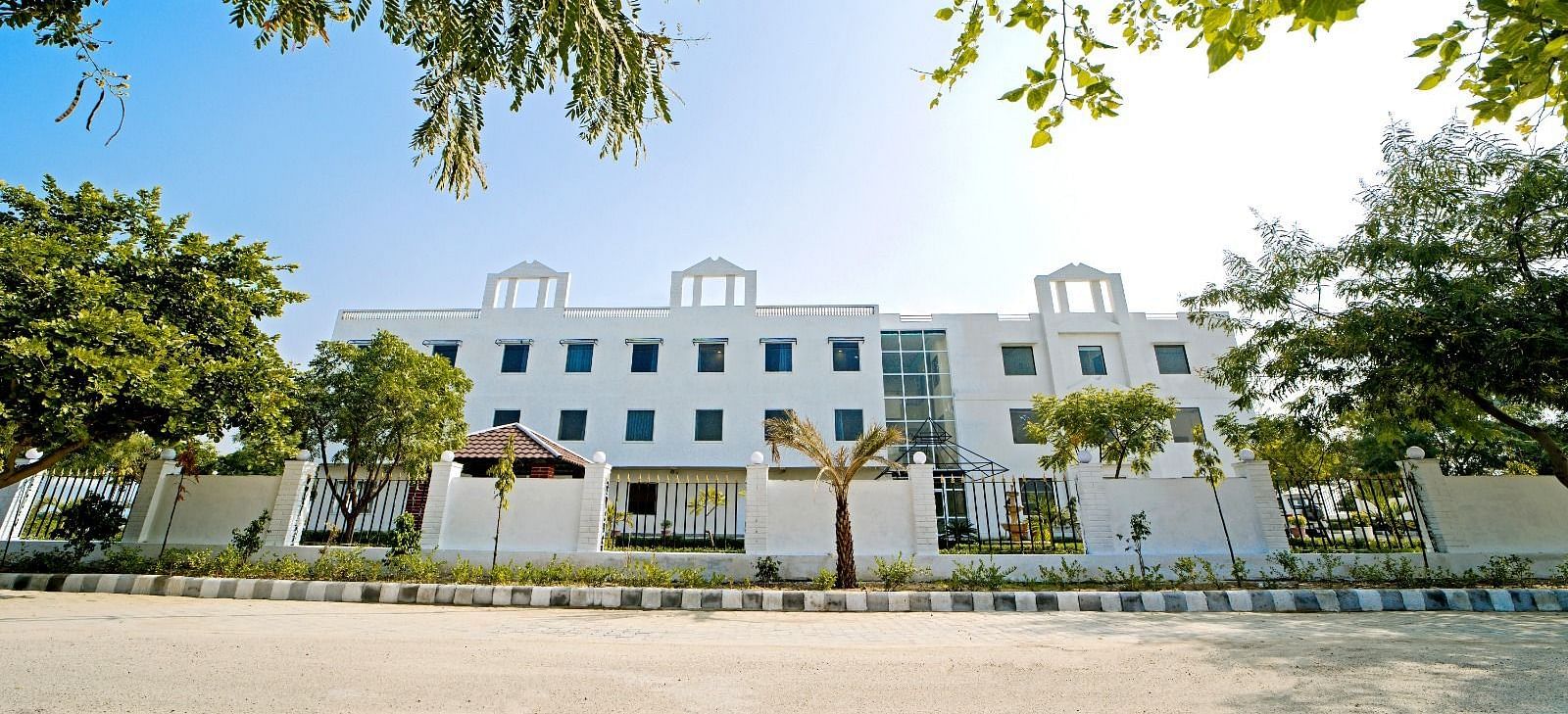 Front view of Grassfield Riveria Resort, Jaipur, surrounded by trees and clear skies, showcasing the modern building facade.