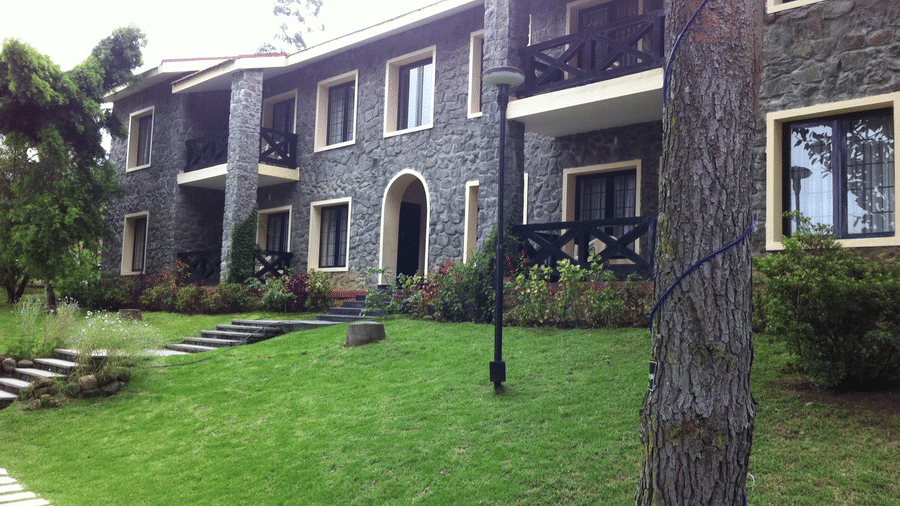 Lawn with stepping stones, trees, and multi-story residential building surrounded by greenery at Green Pastures, Kodaikanal.