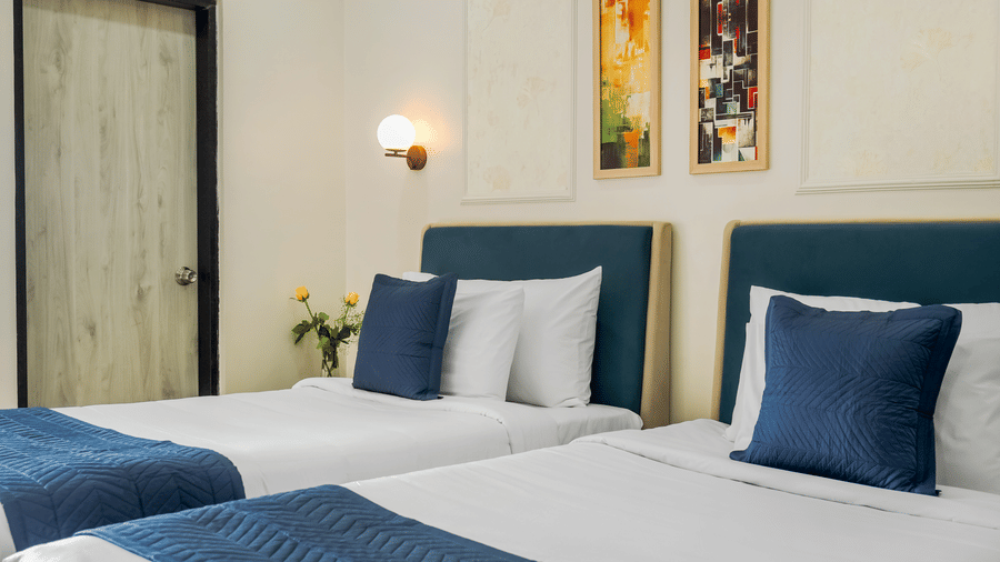 A hotel room at Urban Suites by BluSalzz, Jaipur, featuring two single beds dressed in linens and accents, a wood headboard, and two pictures on the wall.
