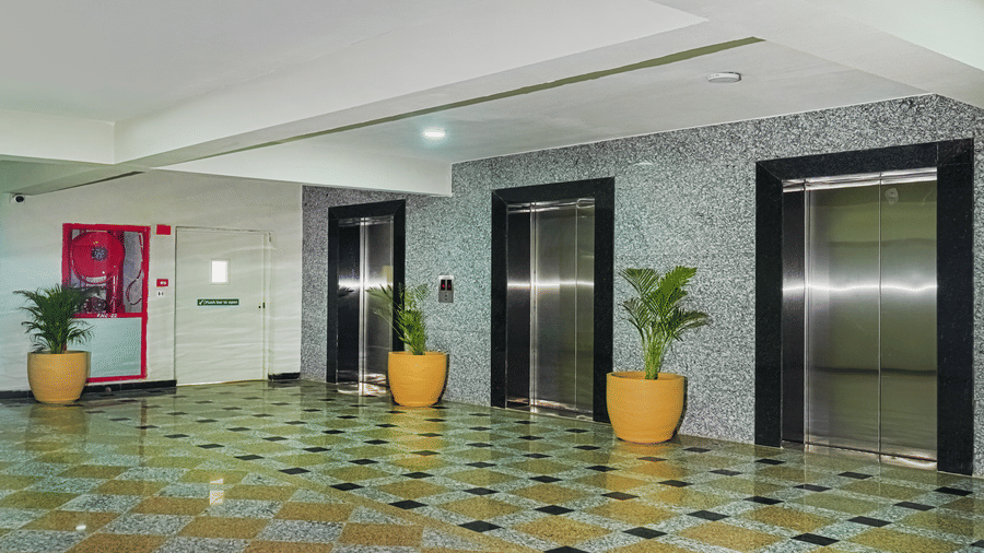 The corridor at Urban Suites by BluSalzz, Jaipur, featuring elevators, plants, and tiled floors.